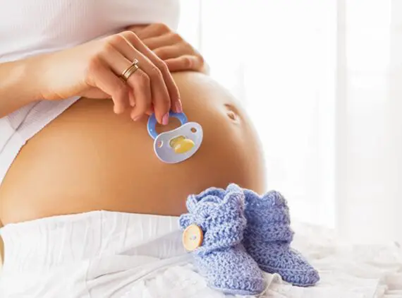 Pregnant woman holding baby shoes and pacifier